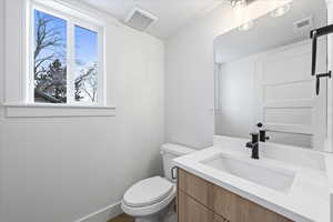 Half bath with baseboards, visible vents, toilet, and vanity