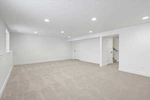 Finished basement with light colored carpet, baseboards, recessed lighting, and a textured ceiling