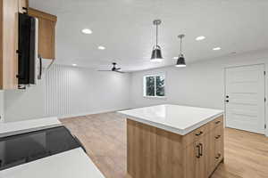 Kitchen featuring a textured ceiling, light countertops, light wood finished floors, a kitchen island, and hanging light fixtures