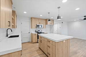 Kitchen featuring light countertops, a sink, light wood finished floors, light brown cabinets, and appliances with stainless steel finishes