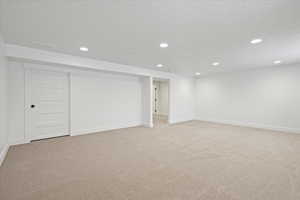 Finished below grade area with a textured ceiling, recessed lighting, and light colored carpet