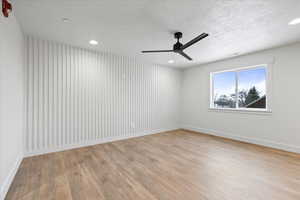 Spare room featuring a textured ceiling, visible vents, light wood-style flooring, baseboards, and a ceiling fan