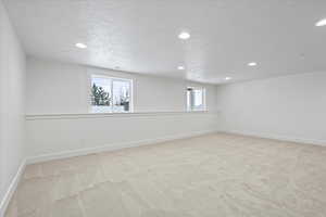 Basement with light carpet, baseboards, recessed lighting, and a textured ceiling