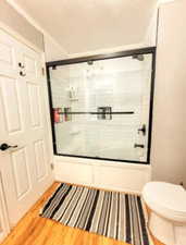 Full bath featuring toilet, bath / shower combo with glass door, and wood finished floors