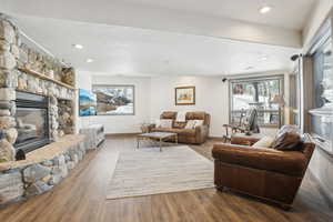 Living room with baseboards, wood finished floors, recessed lighting, and a stone fireplace