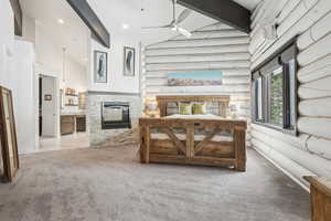 Carpeted bedroom with a stone fireplace, rustic walls, beamed ceiling, high vaulted ceiling, and a wall mounted AC