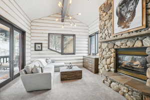Carpeted living room with rustic walls, high vaulted ceiling, wood ceiling, plenty of natural light, and a stone fireplace