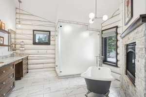 Full bathroom featuring marble finish floor, a freestanding bath, vanity, and a glass covered fireplace