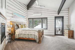 Bedroom with carpet flooring, lofted ceiling with beams, access to exterior, a stone fireplace, and a wall mounted air conditioner