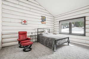 Bedroom with rustic walls, vaulted ceiling, and carpet floors