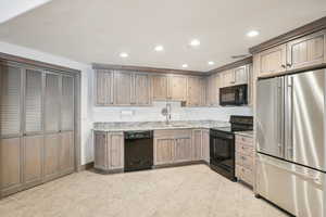 Kitchen with light stone counters, a sink, visible vents, black appliances, and recessed lighting