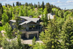View of front of home with stone siding, an attached garage, concrete driveway, a chimney, and roof with shingles