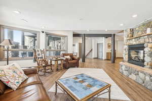 Living room with a stone fireplace, light wood-type flooring, recessed lighting, and stairway