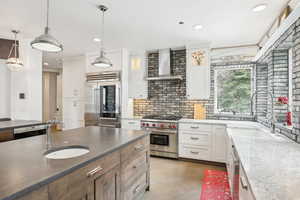Kitchen with wall chimney range hood, premium appliances, a sink, recessed lighting, and white cabinets