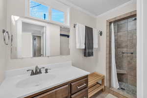 Bathroom featuring vanity, a tile shower, and crown molding