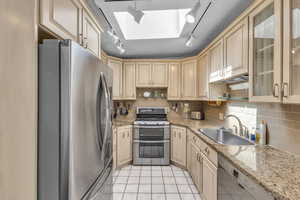 Kitchen with light brown cabinetry, backsplash, a sink, and stainless steel appliances