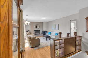 Living room featuring an inviting chandelier, light wood-style floors, a fireplace, and a textured ceiling