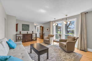 Living area with light wood finished floors, a textured ceiling, baseboards, and an inviting chandelier