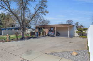 View of front facade featuring an attached carport, driveway, and fence