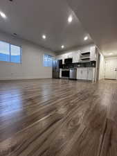 Kitchen featuring open floor plan, dark wood-style floors, white cabinetry, and appliances with stainless steel finishes