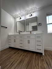 Bathroom with baseboards, double vanity, wood finished floors, and a textured ceiling