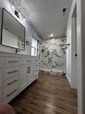 Full bath featuring visible vents, a textured ceiling, vanity, wood finished floors, and a marble finish shower