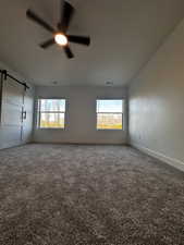 Carpeted spare room with plenty of natural light, a barn door, baseboards, and a ceiling fan