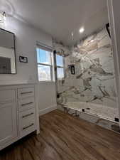 Bathroom with a textured ceiling, wood finished floors, a marble finish shower, and baseboards