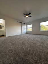 Carpeted empty room with a barn door, visible vents, baseboards, and ceiling fan