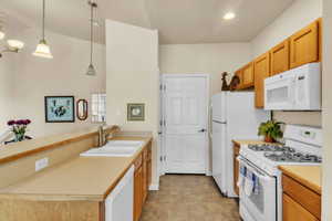 Kitchen with light countertops, a sink, a peninsula, and white appliances
