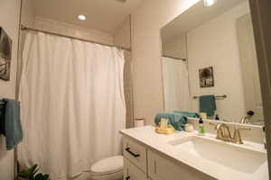 Full bathroom with curtained shower, recessed lighting, toilet, and vanity