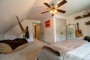 Bedroom with vaulted ceiling, light colored carpet, baseboards, a textured ceiling, and a ceiling fan