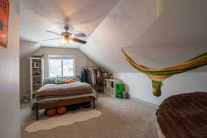 Bedroom featuring vaulted ceiling, carpet flooring, a textured ceiling, visible vents, and ceiling fan