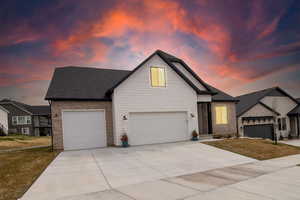 View of front of house featuring an attached garage, a lawn, brick siding, driveway, and a shingled roof