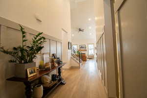 Corridor featuring light wood finished floors, baseboards, recessed lighting, stairway, and a high ceiling