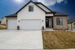 View of front facade featuring a garage, a front yard, brick siding, roof with shingles, and driveway