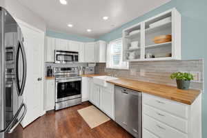 Kitchen featuring backsplash, farmer's sink, wooden counters and stainless steel appliances