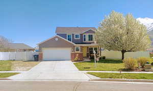 Traditional home with an attached garage, fence, a front lawn, and brick siding