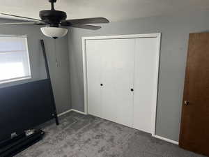 Unfurnished bedroom featuring a closet, a textured ceiling, baseboards, ceiling fan, and dark colored carpet