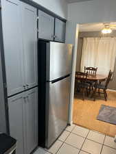 Kitchen with blue cabinetry, ceiling fan, light tile patterned floors, and freestanding refrigerator