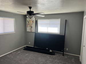 Carpeted empty room with baseboards, a textured ceiling, and a ceiling fan