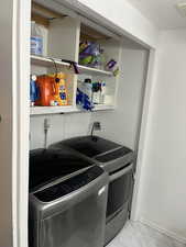 Clothes washing area featuring washing machine and clothes dryer, visible vents, baseboards, marble finish floor, and laundry area