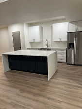 Kitchen with white cabinets, a double waterfall quartz kitchen island, stainless steel refrigerator with ice dispenser, and a sink
