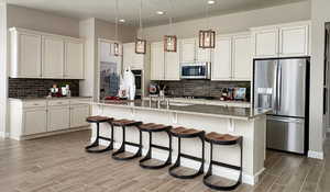 Kitchen featuring backsplash, wood finished floors, a kitchen bar, appliances with stainless steel finishes, and a kitchen island with sink