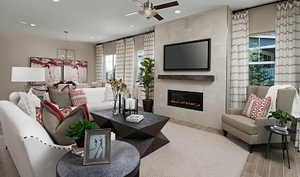 Living area featuring ceiling fan with notable chandelier, recessed lighting, a glass covered fireplace, and wood finished floors