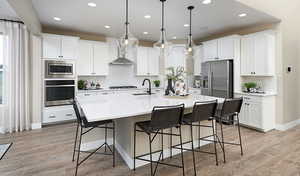 Kitchen with a sink, a breakfast bar area, light wood-style floors, and appliances with stainless steel finishes