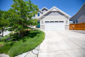View of front of property with board and batten siding, an attached garage, driveway, and stone siding