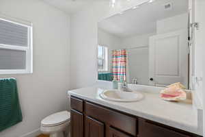 Bathroom featuring a shower with curtain, toilet, vanity, and visible vents