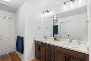 Full bath with baseboards, double vanity, a sink, and wood finished floors