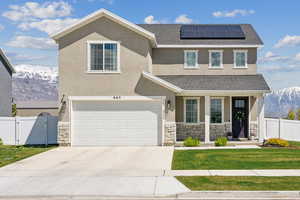 View of front facade with fence, stone siding, roof mounted solar panels, a gate, and a mountain view